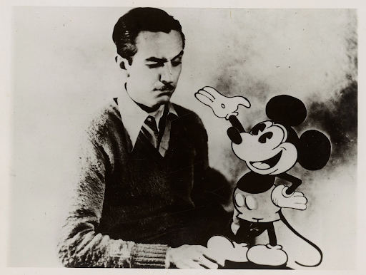 A photograph of Walt Disney with an older drawing of Mickey Mouse. 