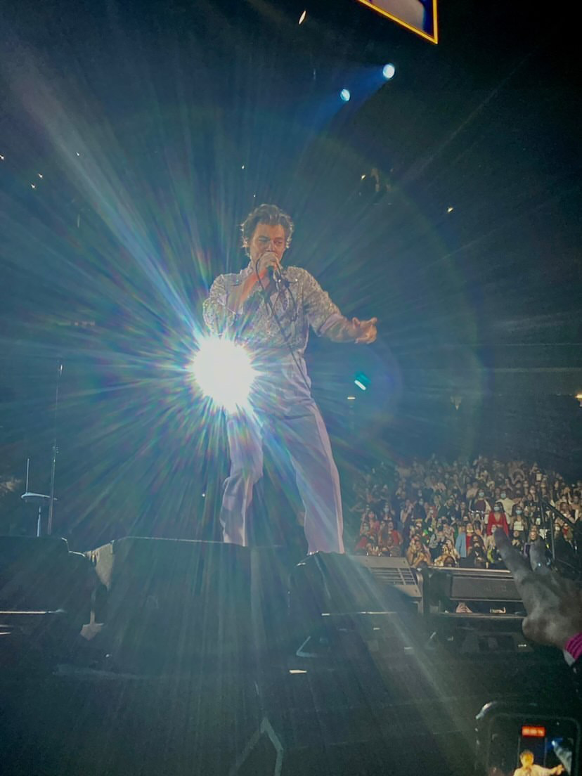 Harry Styles shining on stage whilst engaging with  fans in the pit.